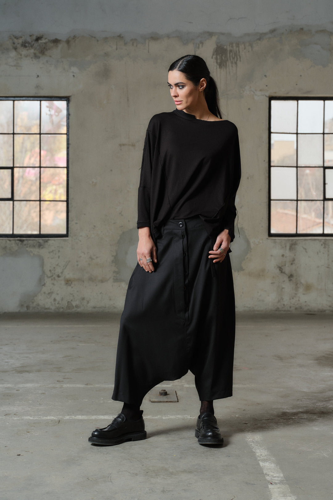 A woman models a dark navy two-piece suit consisting of a tailored blazer and matching relaxed trousers, paired with black platform boots, standing in front of a modern glass window.