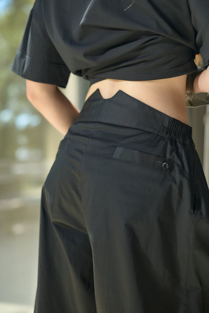 Close-up of a person wearing black wide-leg trousers with an elastic waistband and a small side button detail, paired with a black cropped top.