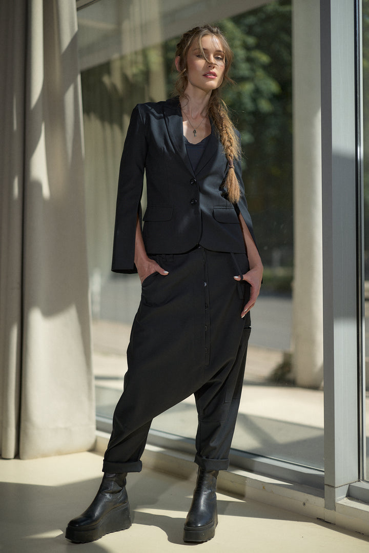 A woman models a dark navy two-piece suit consisting of a tailored blazer and matching relaxed trousers, paired with black platform boots, standing in front of a modern glass window.