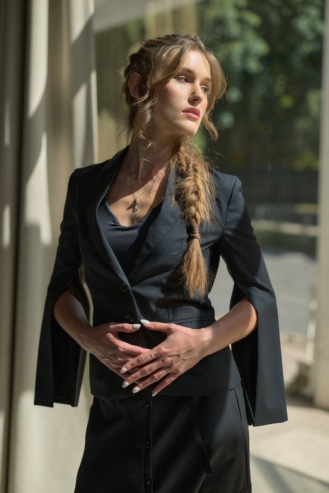 A woman wearing a dark navy blue tailored blazer and matching skirt, standing in front of a sunlit building with columns.