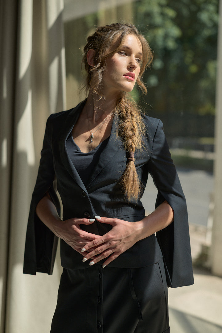 A woman wearing a dark navy blue tailored blazer and matching skirt, standing in front of a sunlit building with columns.