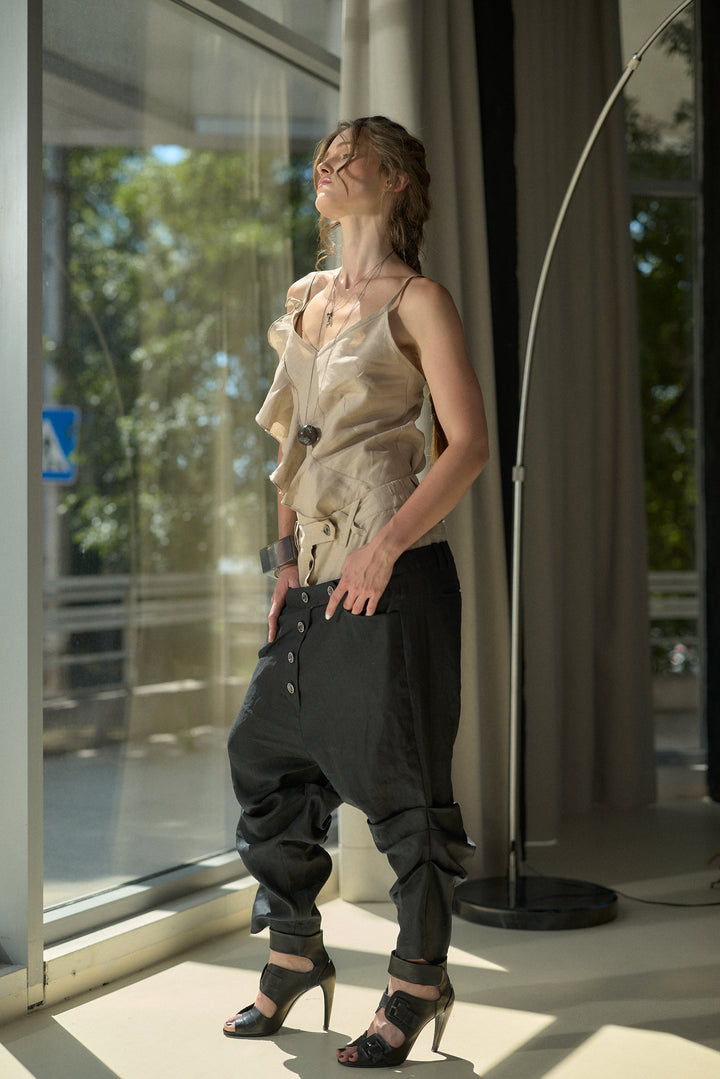 A woman models a two-piece outfit consisting of a beige ruffled camisole top and black baggy pants with cuffed hems, standing in a brightly lit room with large windows.