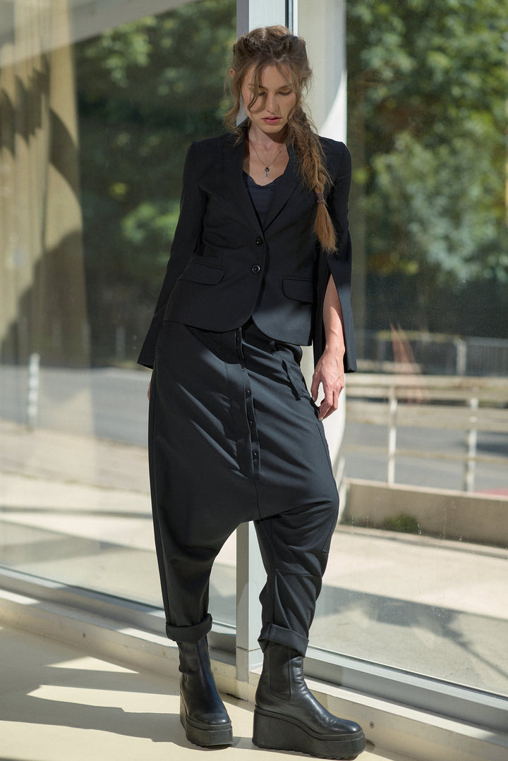 A woman models a black two-piece outfit consisting of a cropped blazer and matching baggy pants with platform boots, standing in front of a glass window.
