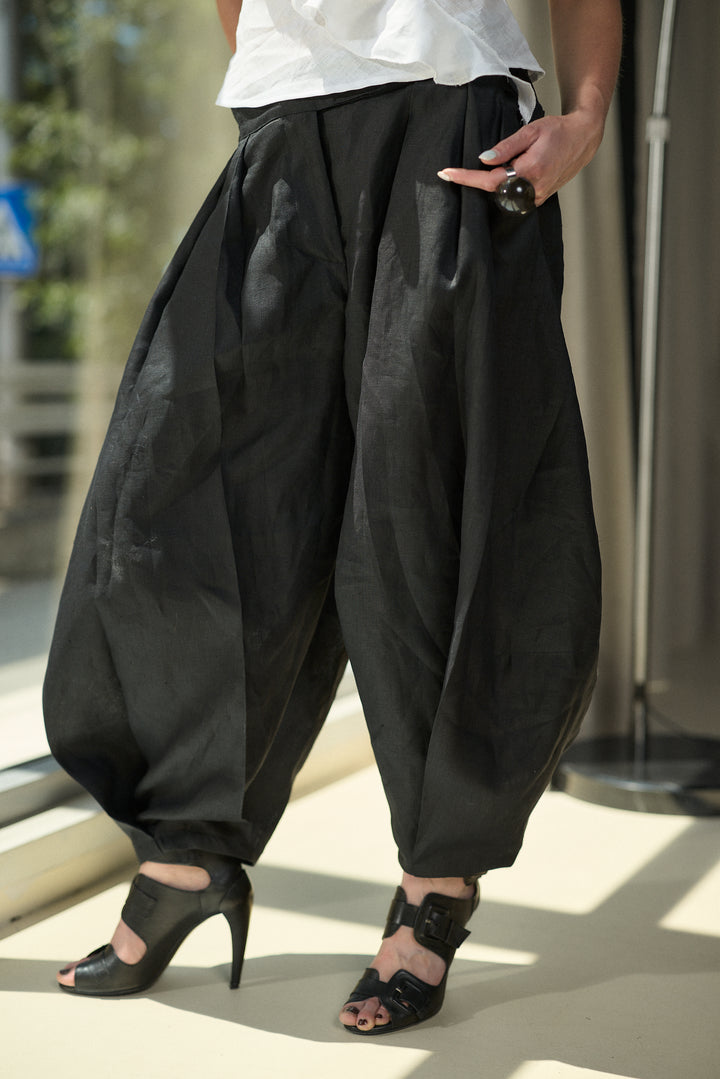A person wearing voluminous black balloon-style pants with a white top and black high-heeled sandals, photographed outdoors in bright sunlight.