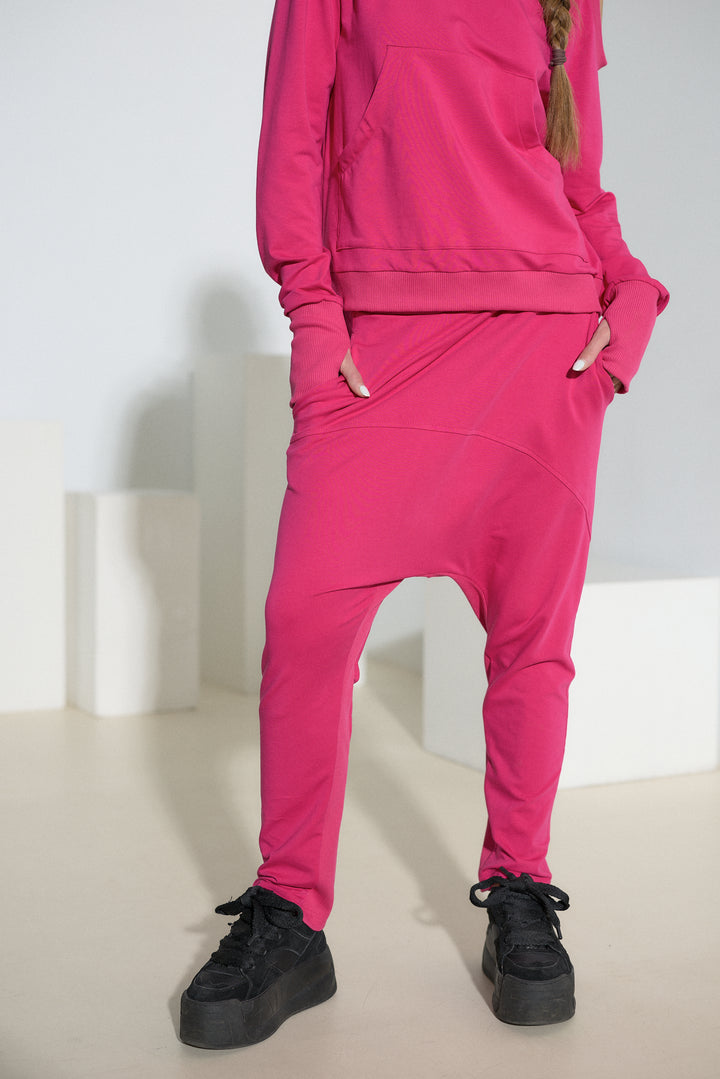 A model wearing a bright pink two-piece lounge set consisting of a sweatshirt and matching baggy jogger pants, paired with black platform sneakers.